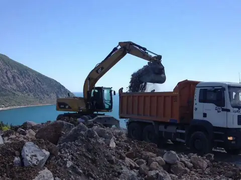Экскаватор грузит самосвал у береговой линии